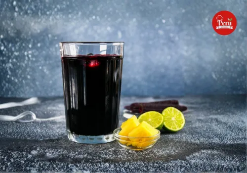 Chicha Morada Peruana: Receta Tradicional y Auténtica | La Bebida de los Incas vaso de chicha morada peruana con limón verde y trozos de piña al lado sobre una mesa.